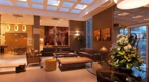 Un hall d’hôtel moderne, doté d’un plafond haut, d’un espace salon central et d’une grande fenêtre offrant une vue sur l’extérieur.