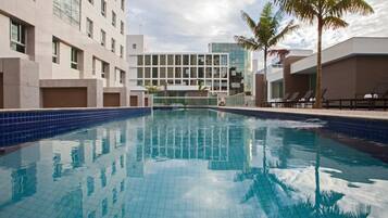 A swimming pool with clear blue water, surrounded by modern buildings and palm trees.