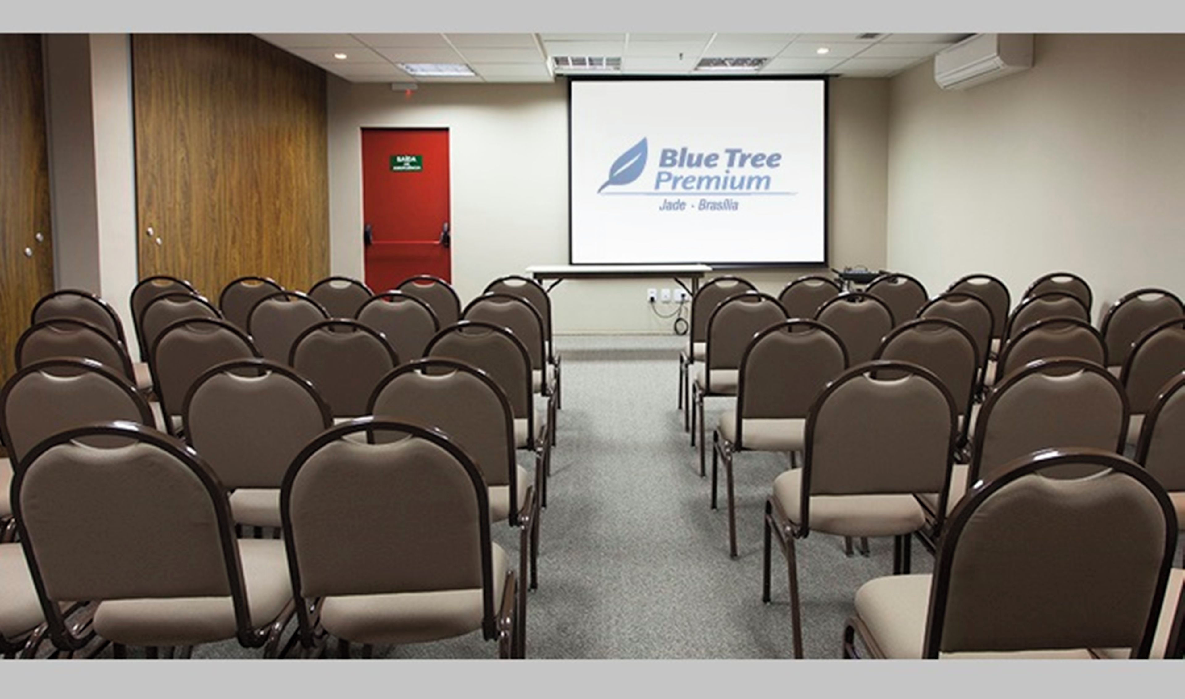 A conference room with rows of chairs, a projector screen displaying 'Blue Tree Premium,' and a red door.