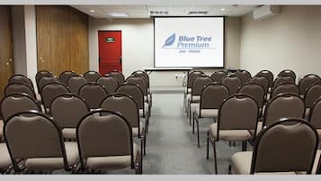 A conference room with rows of chairs, a projector screen displaying 'Blue Tree Premium,' and a red door.