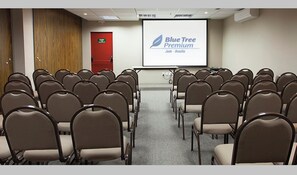 A conference room with rows of chairs, a projector screen displaying 'Blue Tree Premium,' and a red door.