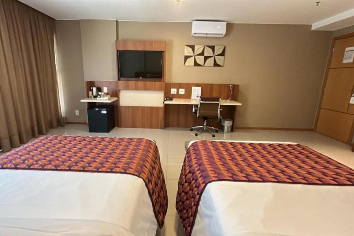 A hotel room with two beds, a desk, a chair, a television, and a wardrobe.