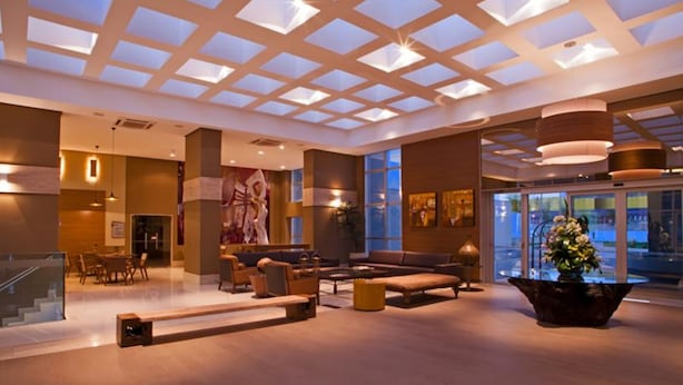 Eine geräumige Lobby mit hoher Decke, großen Fenstern und einer zentralen Sitzgelegenheit.
