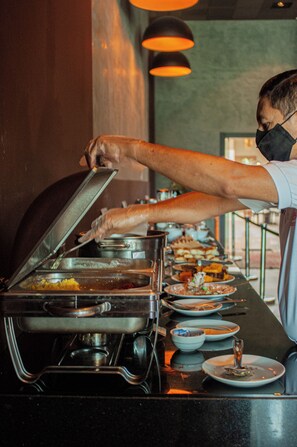 A buffet setup with multiple food stations and a person serving food. - Jade Hotel (Guará)