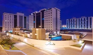 Un moderno complejo hotelero con varios edificios altos, una piscina y una zona ajardinada con palmeras.