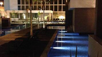 A nighttime view of a hotel pool area with a water feature, palm trees, and a building in the background.