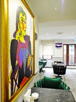A hotel lobby with a large abstract painting, a reception desk, a television, and a dining area with green chairs and a marble table. - Hub Inn Pera (Istanbul)