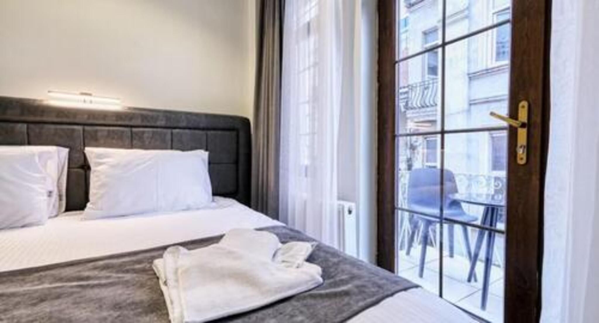 A hotel room with a bed, a window with a view of the street, and a door with a handle.