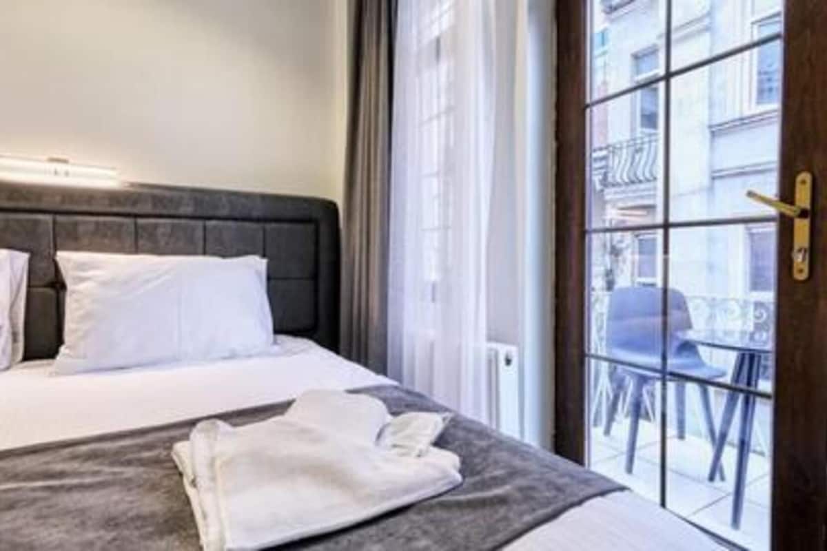 A hotel room with a bed, a window with a view of the street, and a door with a handle.