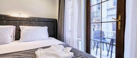 A hotel room with a bed, a window with a view of the street, and a door with a handle.