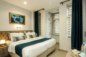 A hotel room with a bed, bedside table, lamp, artwork, and a window with blinds. - Hub Inn Pera (Istanbul)