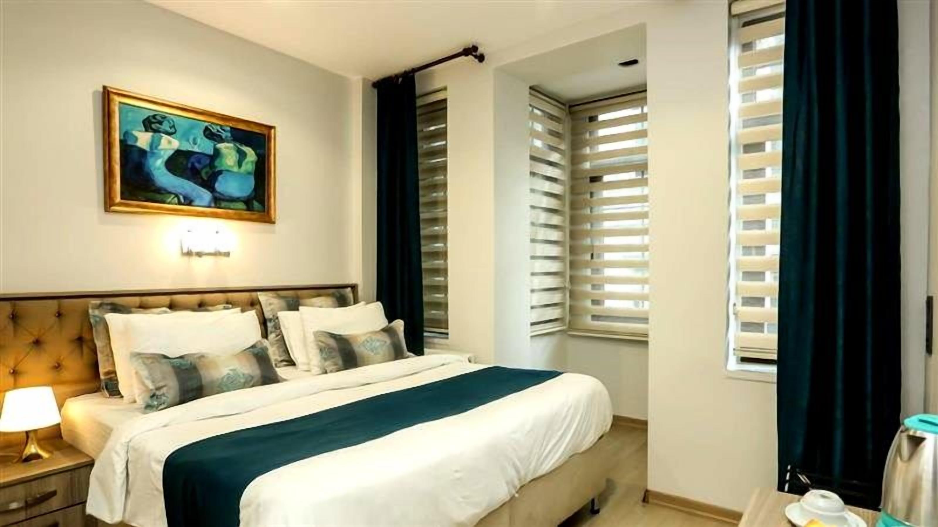 A hotel room with a bed, a nightstand, a lamp, and a painting on the wall.