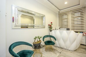 A reception area with a white reception desk, two green chairs, a small table with a potted plant, and a large mirror on the wall. - Hub Inn Pera (Istanbul)