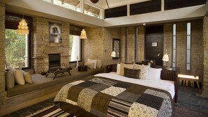 A spacious bedroom with a large bed, stone walls, a fireplace, and a ceiling fan.