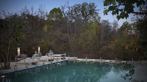 A serene outdoor pool area with a lounge chair and a small table, surrounded by trees.