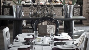 A dining area with a table set for two, a chandelier, and a brick wall with shelves in the background.