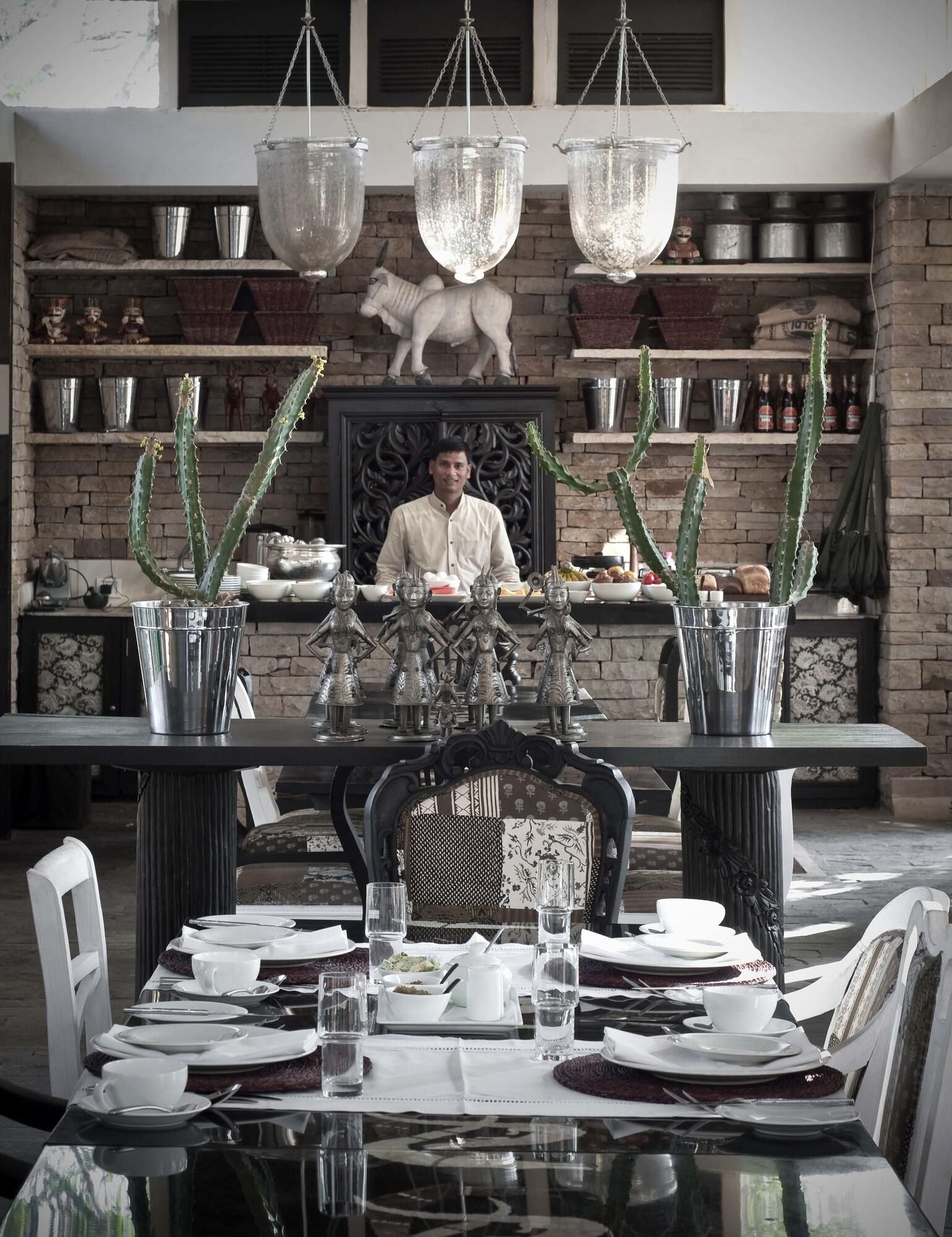 Un coin repas avec une table dressée pour deux personnes, un mur décoratif agrémenté d’étagères et des luminaires suspendus.