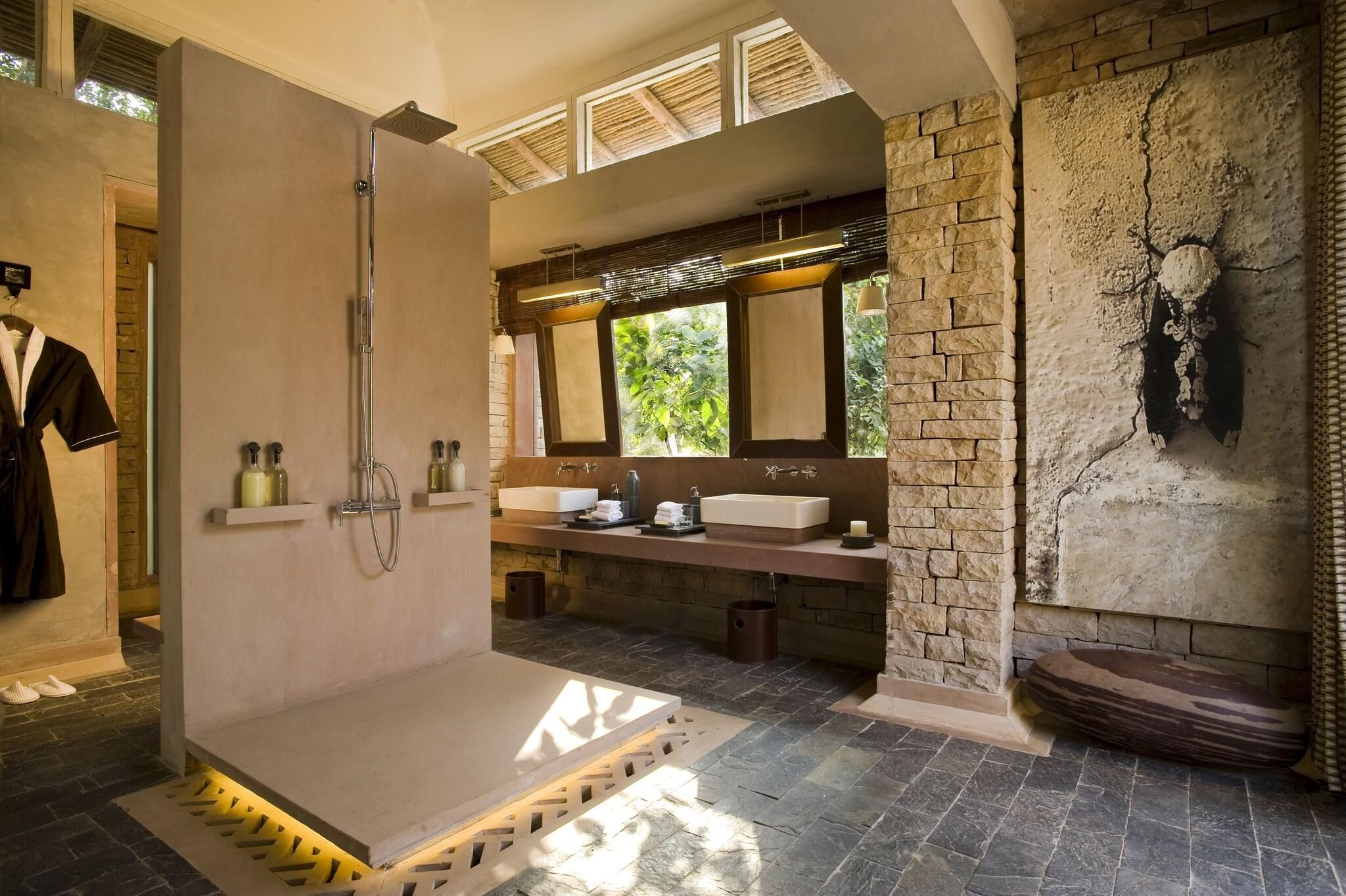 Une salle de bain moderne avec une douche, deux lavabos, un grand miroir et un mur en pierre.