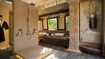 Une salle de bain moderne avec une douche, deux lavabos, un grand miroir et un mur en pierre.
