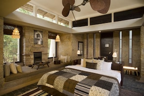 A spacious bedroom with a large bed, a fireplace, and a stone wall.