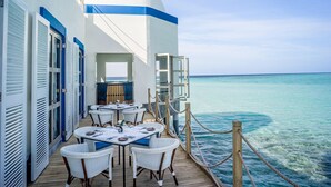 A deck with tables and chairs, overlooking a clear blue sea. - Intercontinental Maldives Maamunagau Resort (Maamunagau Island)