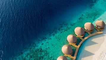 An aerial view of a resort with overwater bungalows connected by a wooden walkway.