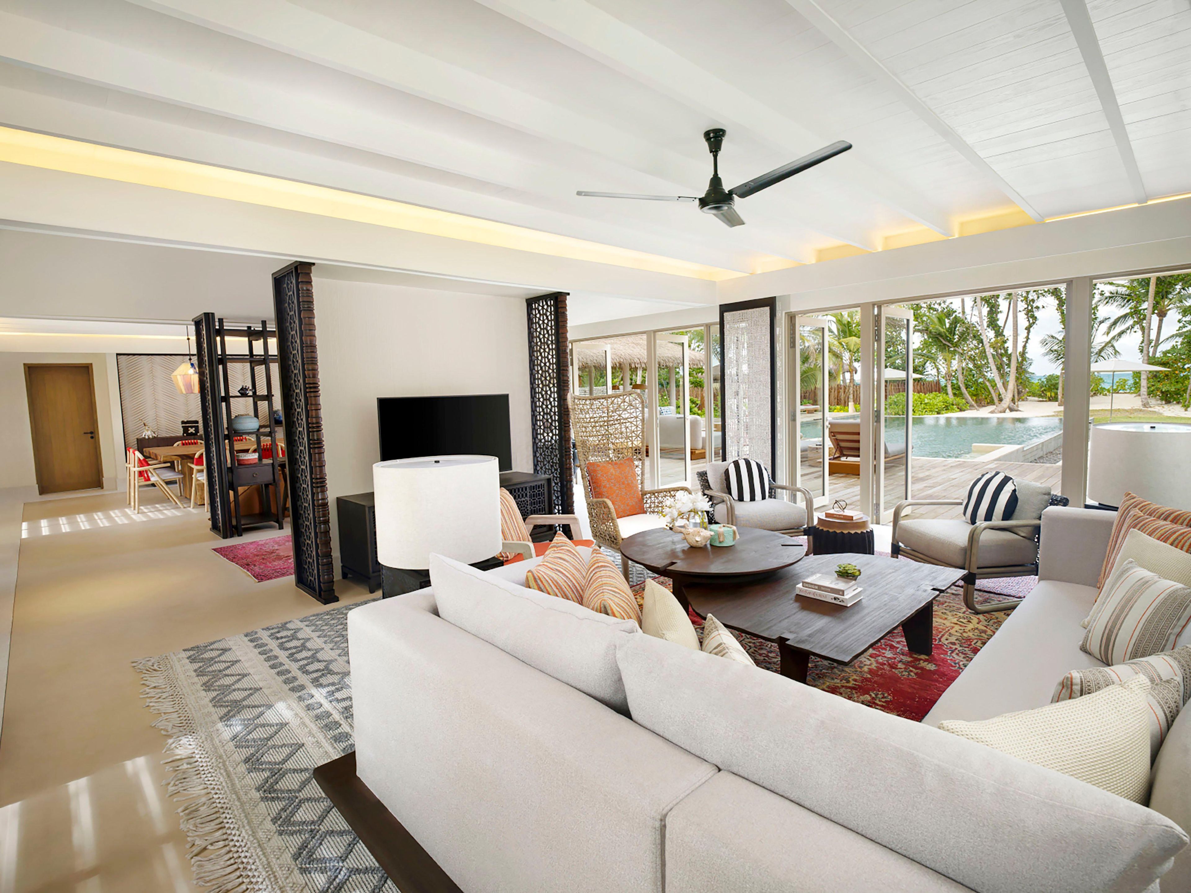 A spacious living room with a large sofa, a coffee table, and a TV. There is a balcony with a pool view.