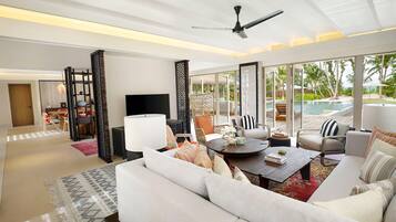 A spacious living room with a large sofa, a coffee table, and a TV. There is a balcony with a pool view.