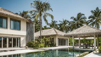 Un resort con piscina, construcciones de techo de paja y palmeras.