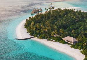 An aerial view of a tropical island with a white sandy beach, clear turquoise waters, and lush green palm trees. - Intercontinental Maldives Maamunagau Resort (Maamunagau Island)