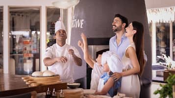 A family in a kitchen with a pizza oven, a child, and a chef.