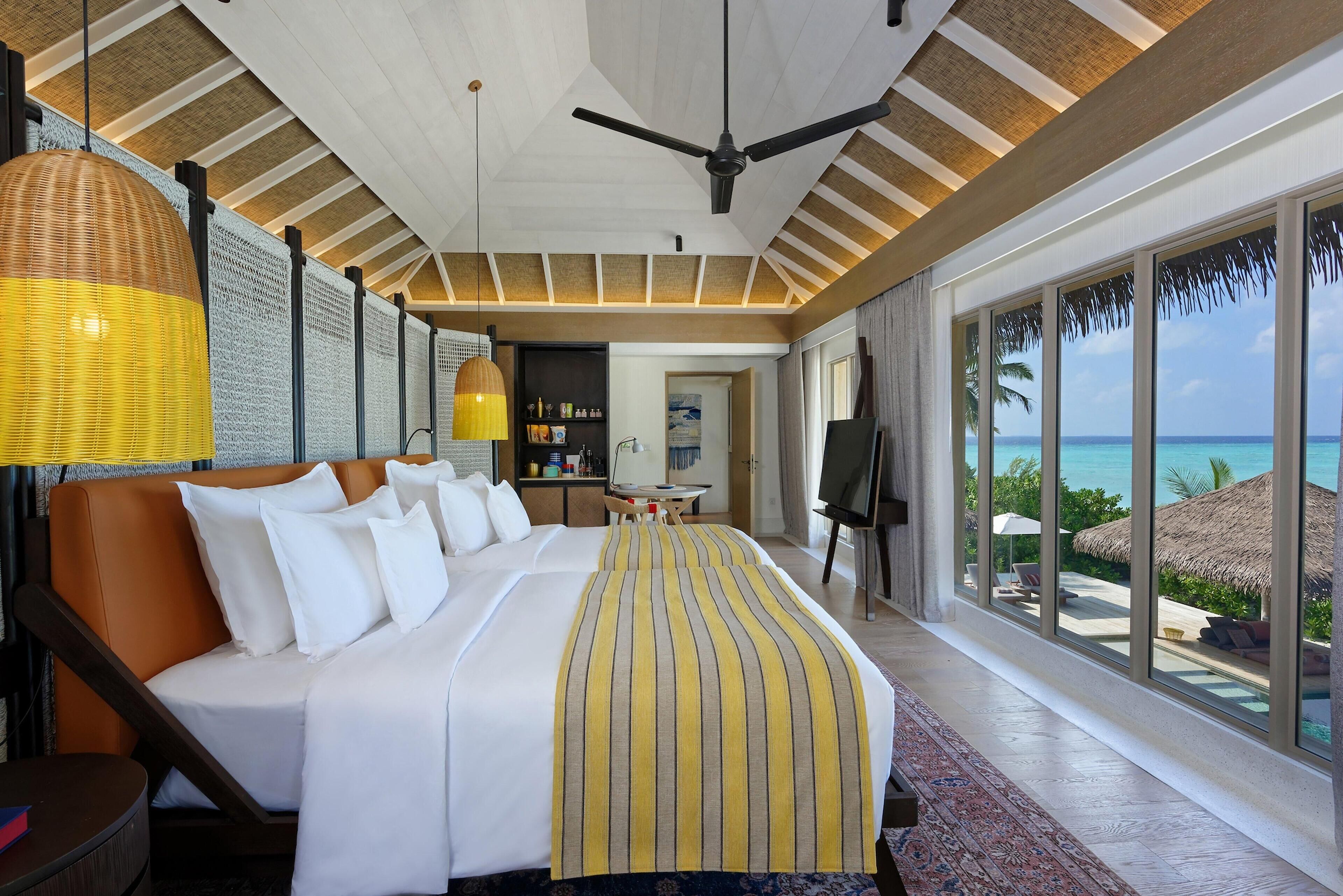 Une chambre d’hôtel avec un grand lit, un ventilateur de plafond, un coin repas et une vue sur l’océan.