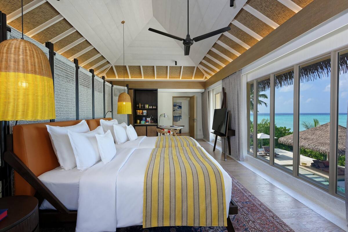 Quarto de hotel com uma cama grande, ventoinha no teto, área de refeições e vista para o oceano.