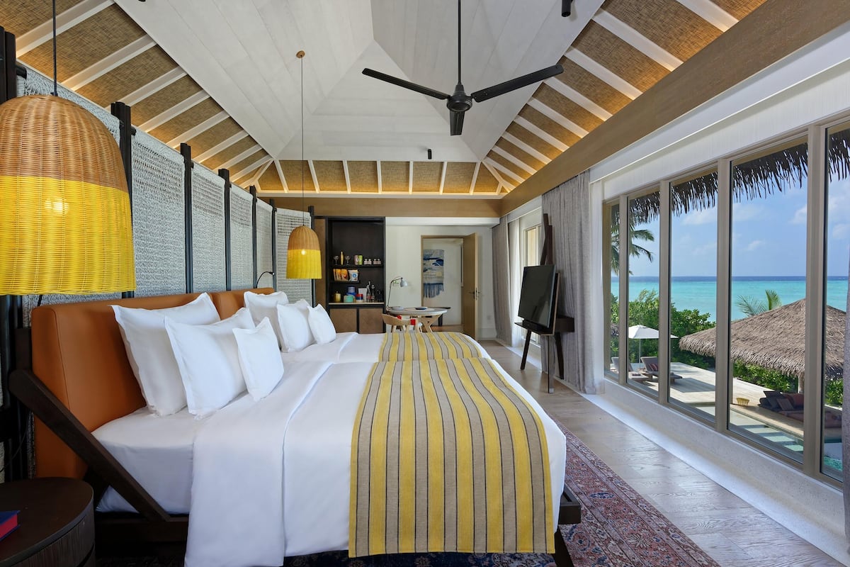 Une chambre d’hôtel avec un grand lit, un ventilateur de plafond, un coin repas et une vue sur l’océan.