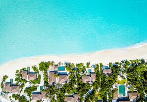 Eine Luftaufnahme eines Strandanliegers mit mehreren Bungalows, jeweils mit eigenem Pool, umgeben von üppiger Vegetation und einem Sandstrand.