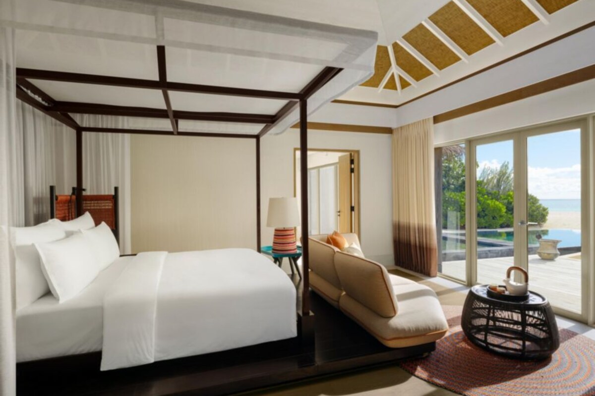 A hotel room with a bed, a sofa, a small table with a lamp, a decorative item, and a view of the outdoors.