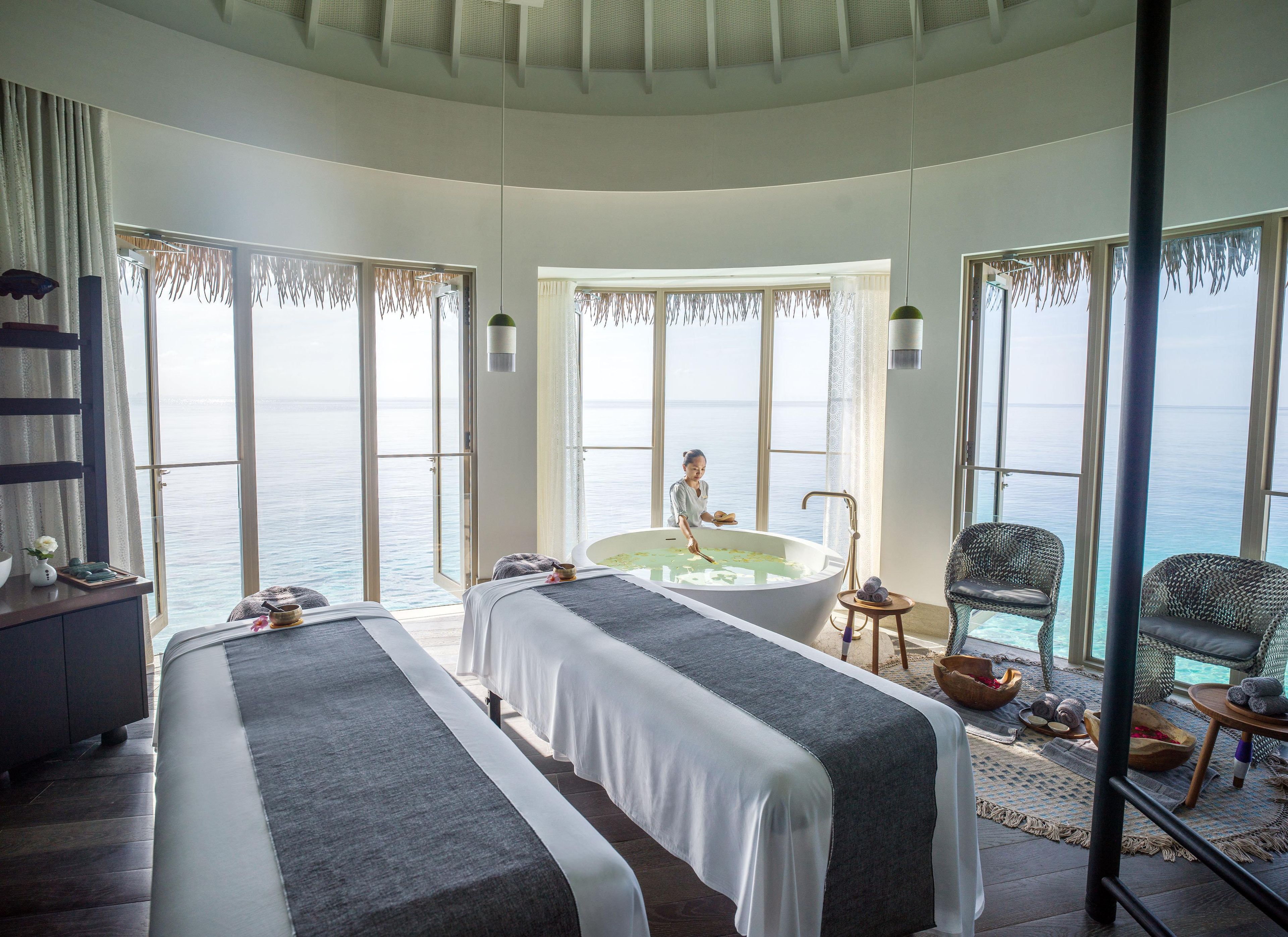 A room with two beds, a bathtub, and a view of the sea.