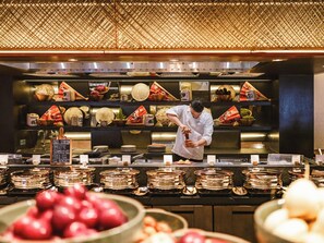 A chef preparing food in a kitchen with traditional decor and a variety of dishes displayed on shelves. - Intercontinental Maldives Maamunagau Resort (Maamunagau Island)