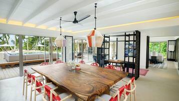 A spacious dining area with a large wooden table, white chairs with red accents, and a ceiling fan.
