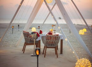 A beachside dining setup with a table, chairs, and string lights.
