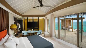 Habitación de hotel con cama, televisor, zona de estar con sillones y vista al océano.