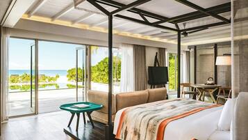 Habitación de hotel con una cama grande, televisión, zona de comedor y vista al océano.