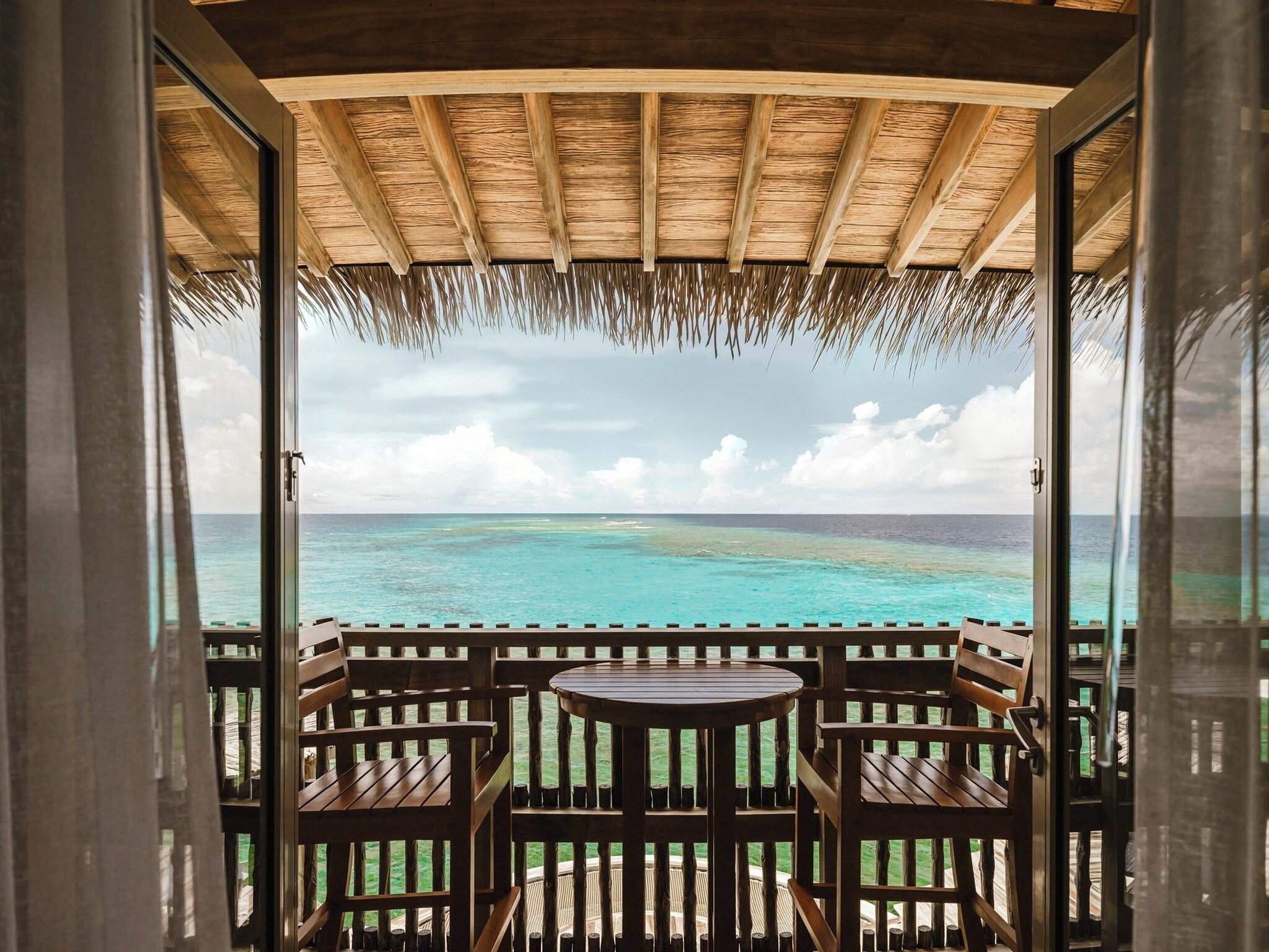 A wooden deck with a thatched roof, overlooking a turquoise sea and a cloudy sky.