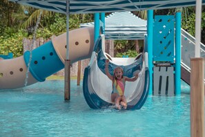 Un toboggan aquatique dans un parc aquatique, avec une glissière bleue et blanche, un auvent rayé bleu et blanc, et une zone de piscine.