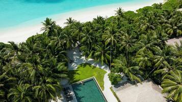 An aerial view of a tropical resort with a pool area surrounded by palm trees and a beach.
