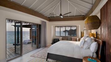 A bedroom with a bed, a ceiling fan, a view of the sea, and a large window.