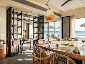 A dining area with a view of the ocean, wooden furniture, and a hanging light fixture.