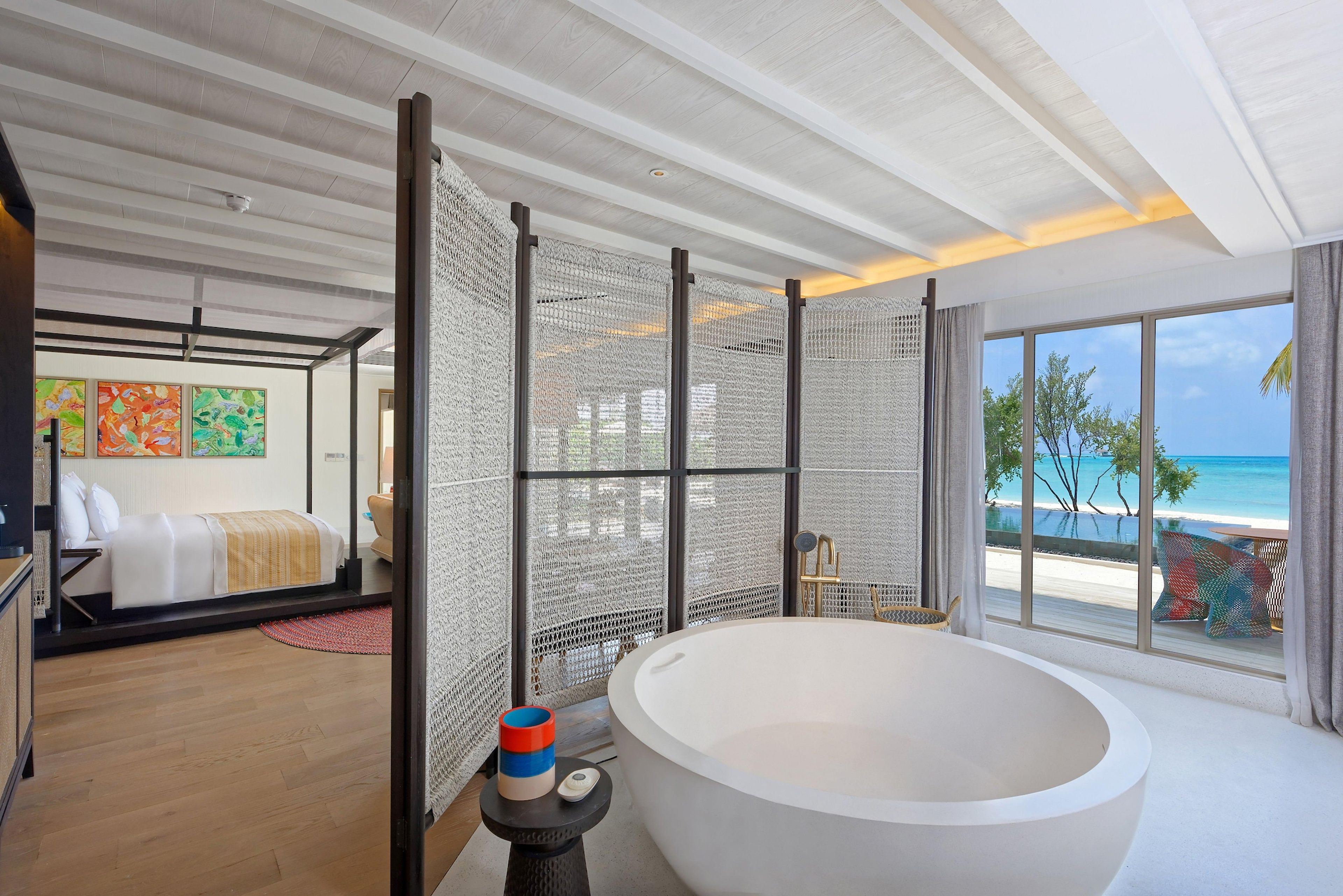 A modern bathroom with a large bathtub, a shower area, and a view of the beach.