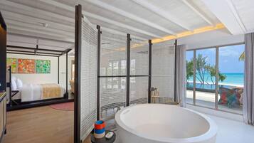 A modern bathroom with a large bathtub, a shower area, and a view of the beach.