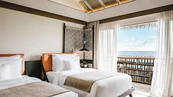 A hotel room with two beds, a ceiling fan, a view of the sea, and a balcony with a wooden railing.